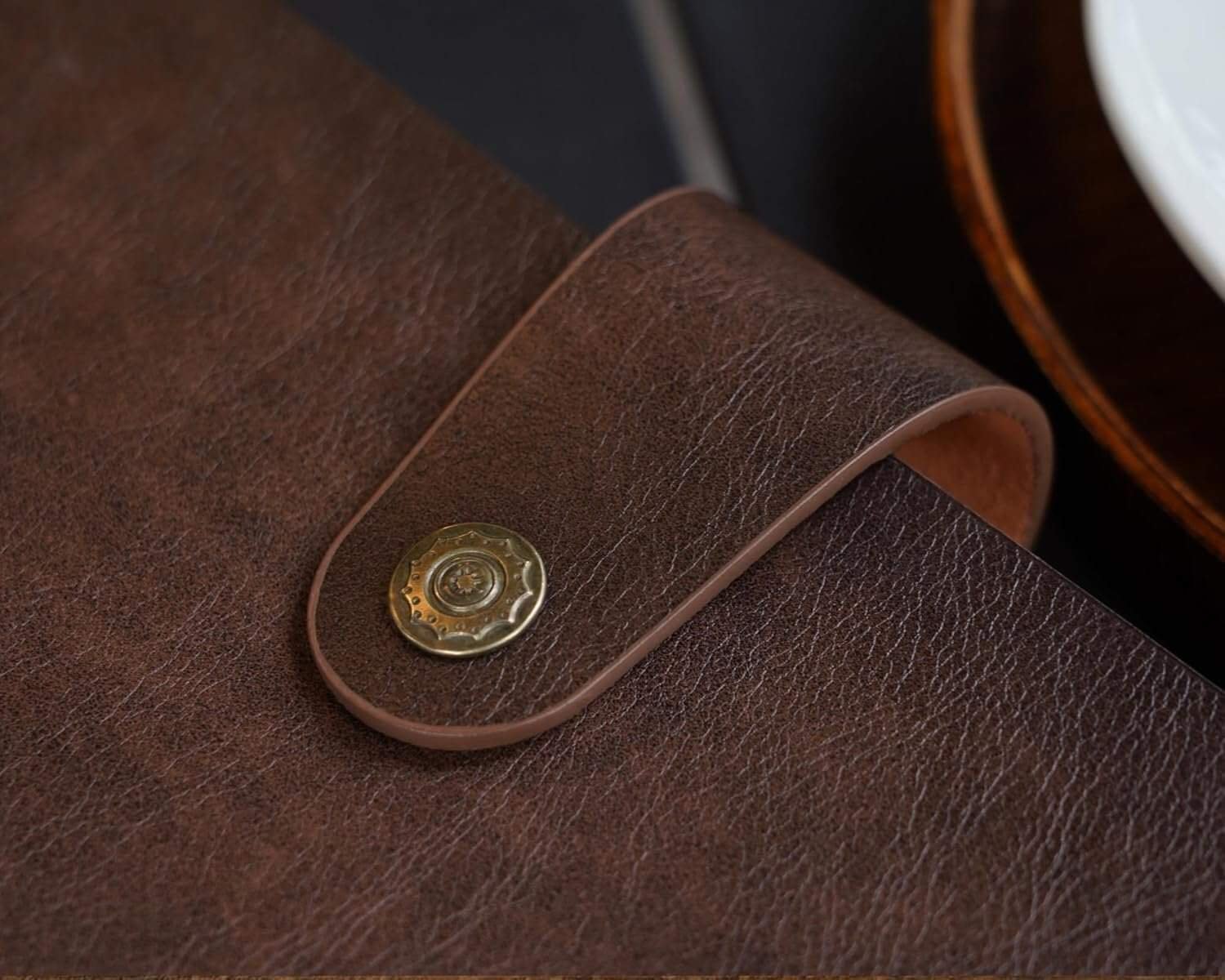 Close-up of a brown leather flap with a brass snap button, showing detailed texture and stitching.