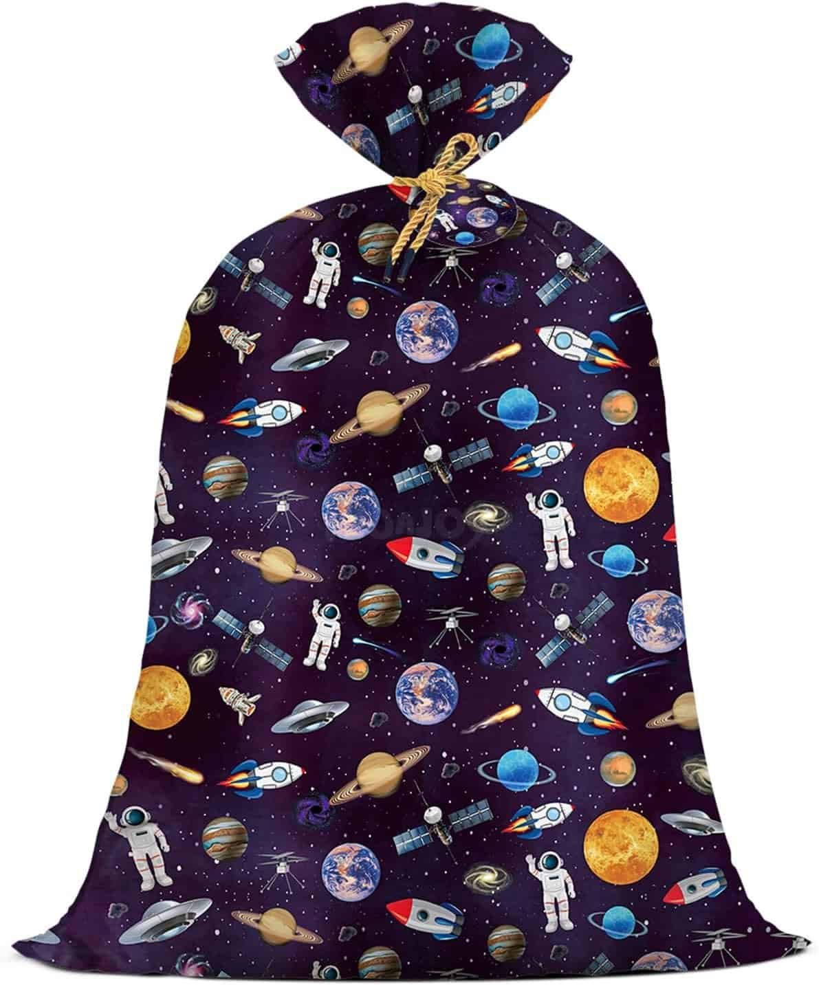 A gift bag decorated with colorful illustrations of astronauts, rockets, planets, satellites, and stars on a dark background.