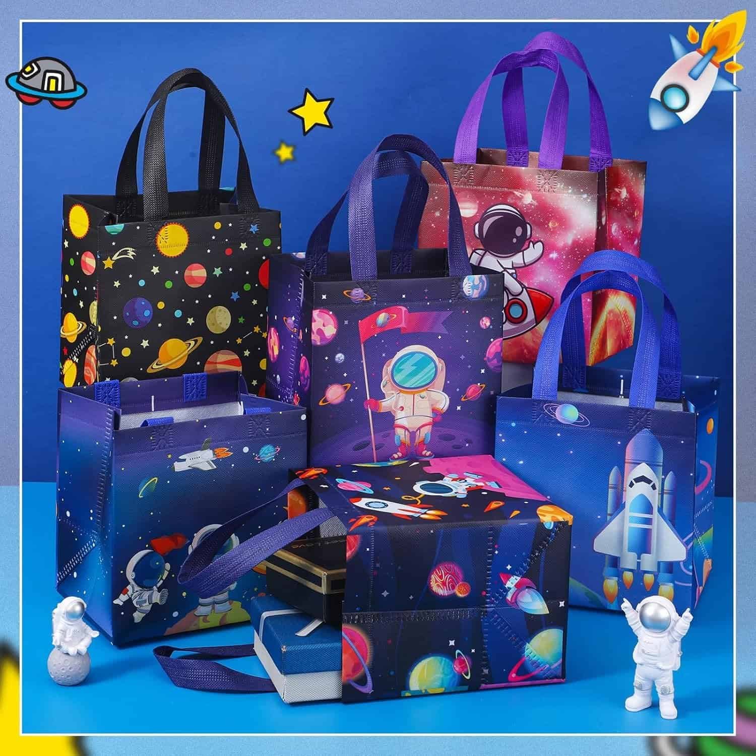 Six colorful reusable bags with space-themed designs, including astronauts, rockets, and planets, are arranged on a blue surface with two small astronaut figurines and some books.