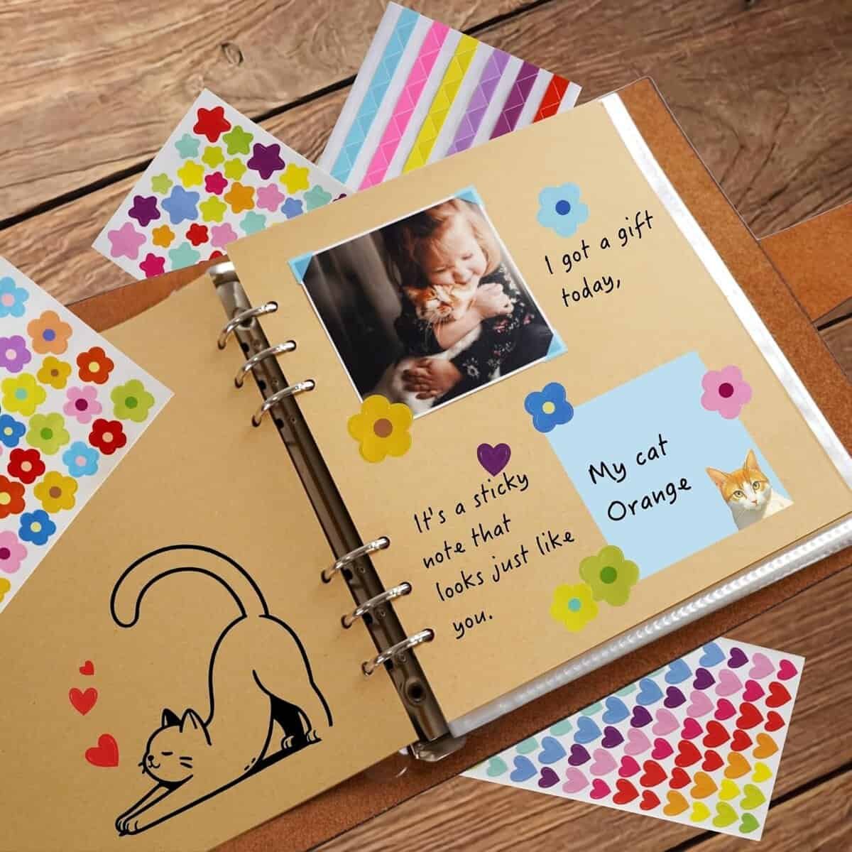 An open scrapbook features a photo of a cat and decorated pages with colorful stickers, a drawing of a cat, and handwritten notes about a gift and a cat named Orange.