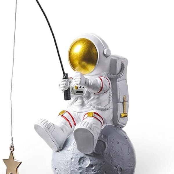 A figurine of an astronaut sitting on a small moon, holding a fishing pole with a dangling gold star attached to the line.