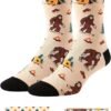 Pair of beige socks with black cuffs featuring cartoon Bigfoot, tents, campfires, and trees; shown with a polka-dot gift box and a view of the socks folded inside.
