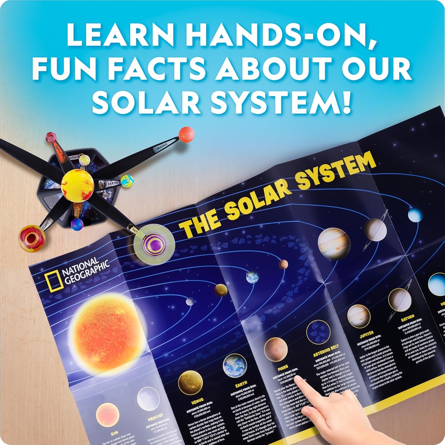 A hand points to a planet on a National Geographic solar system chart, with a solar system model and the text "Learn hands-on, fun facts about our solar system!" above.