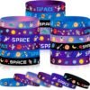 A collection of colorful silicone wristbands with space-themed designs, including astronauts, rockets, planets, and stars, arranged in stacks and rows.