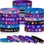 A collection of colorful silicone wristbands with space-themed designs, including astronauts, rockets, planets, and stars, arranged in stacks and rows.