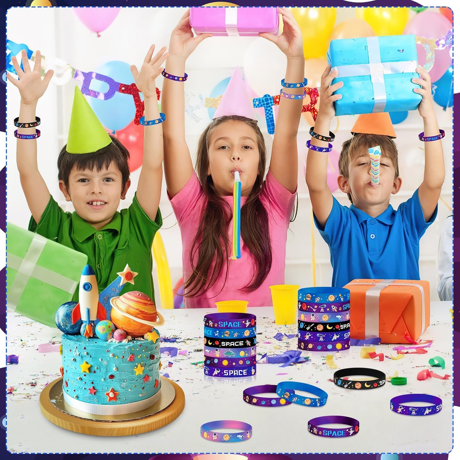 Three children wearing party hats celebrate at a table with a space-themed cake, wrapped gifts, balloons, and assorted party favors including colorful bracelets.