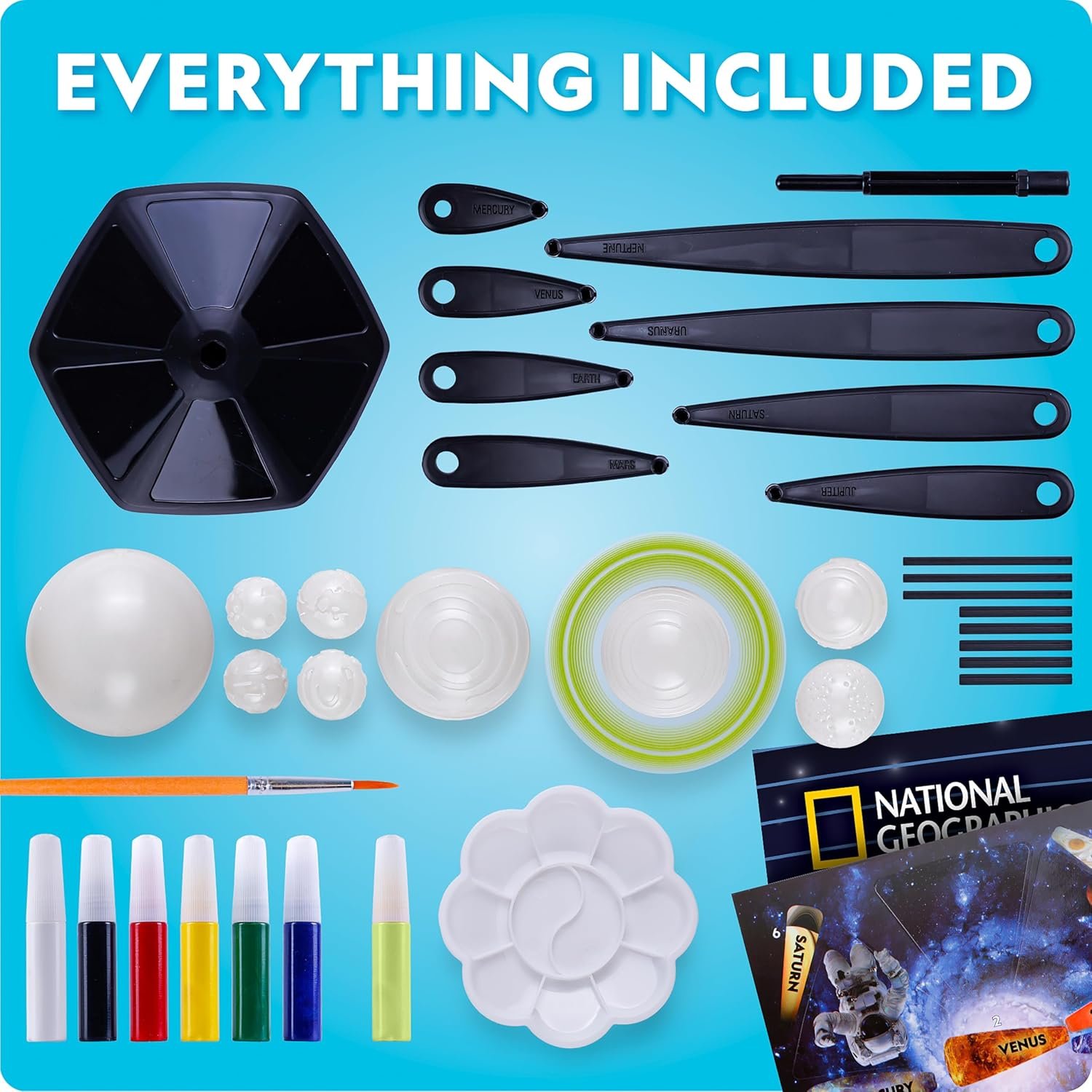 Art and science kit contents including paintbrush, paint pots, sculpting tools, mixing tray, plastic domes, and National Geographic activity booklet arranged on a blue background.