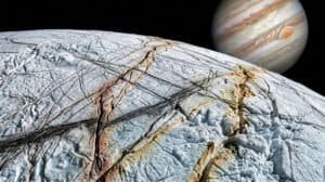 A close-up view of Europa’s cracked, icy surface—hinting at traces of ammonia on Europa—with Jupiter and its cloud bands visible in the background in space.