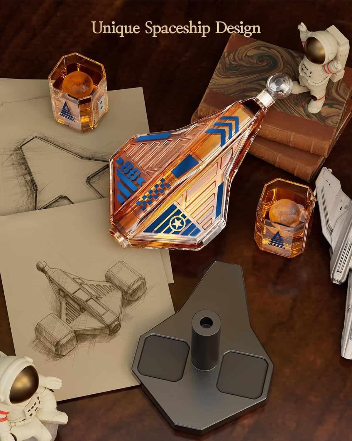 A spaceship-shaped decanter with two glasses, spaceship sketches, a stand, books, and small astronaut figurines on a wooden table. Text reads "Unique Spaceship Design.