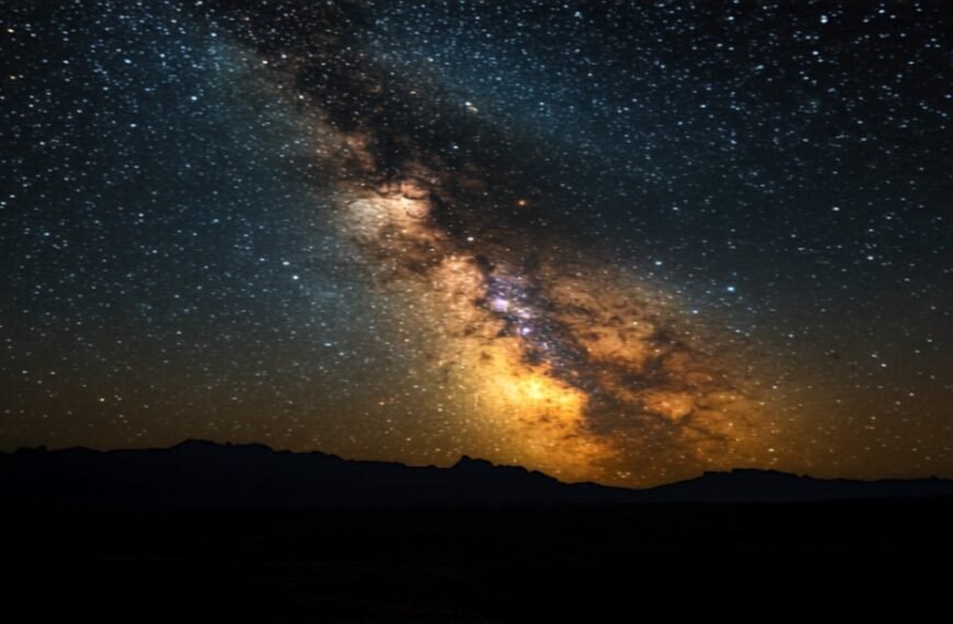 Milky Way galaxy arc glowing over dark rugged landscape at night
