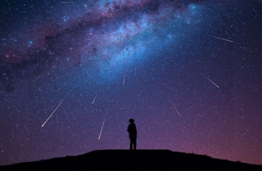 Silhouette of a person standing on a hill at night, gazing up at a star-filled sky with the Milky Way and a mesmerizing meteor shower streaking across the darkness.