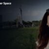 A woman stands outdoors in front of a rocket display, with the Watch Xploration Outer Space | Prime Video logo in the top left corner.