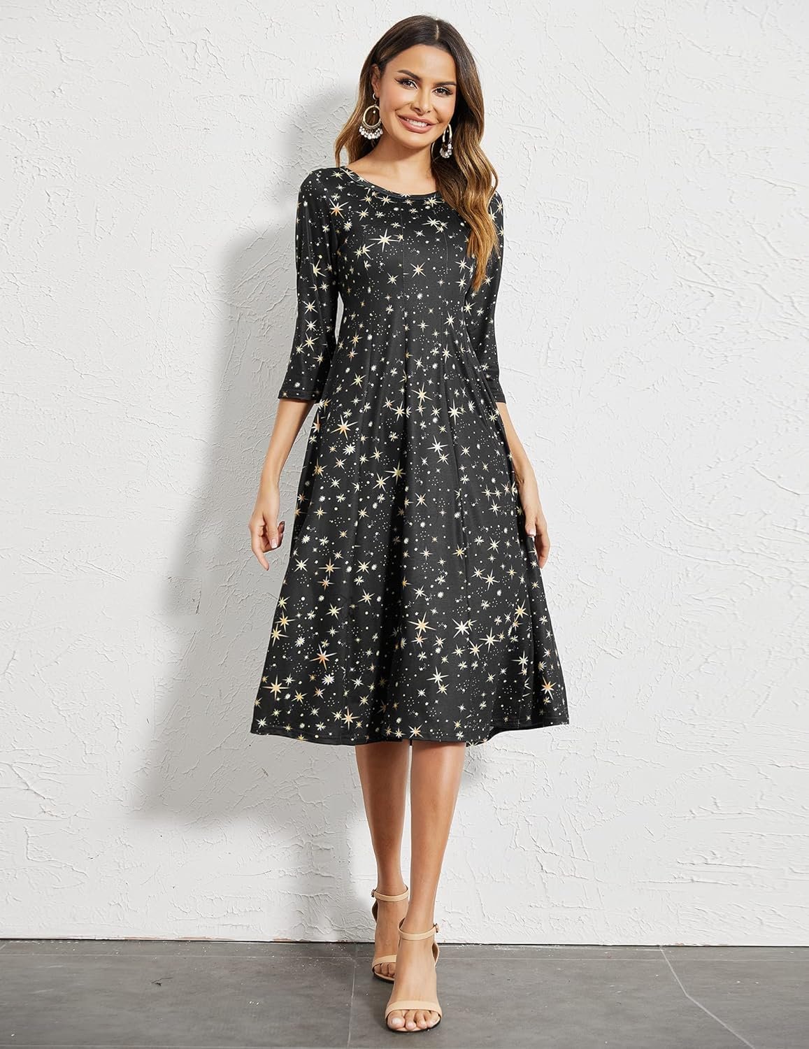 A smiling woman in a starry gown with three-quarter sleeves, standing against a white wall.