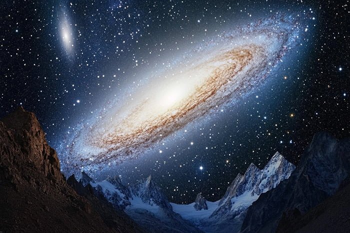 A bright spiral galaxy dominates a star-filled night sky over jagged mountain peaks, with a smaller galaxy visible in the upper left.