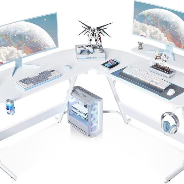 A white L-shaped computer desk setup with two monitors, a mechanical keyboard, a mouse, a computer tower, a model figure, a gaming console controller, headphones, and various accessories.