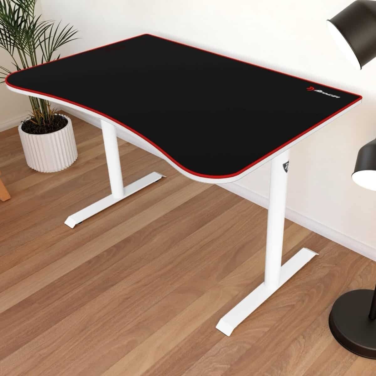 लकड़ी के फर्श वाले कमरे में एक गमले में लगा पौधा, एक फ्लोर लैंप और एक दीवार के कोने में एक घुमावदार मेज रखी है, जिस पर एक काला माउस पैड और सफेद पैर हैं।