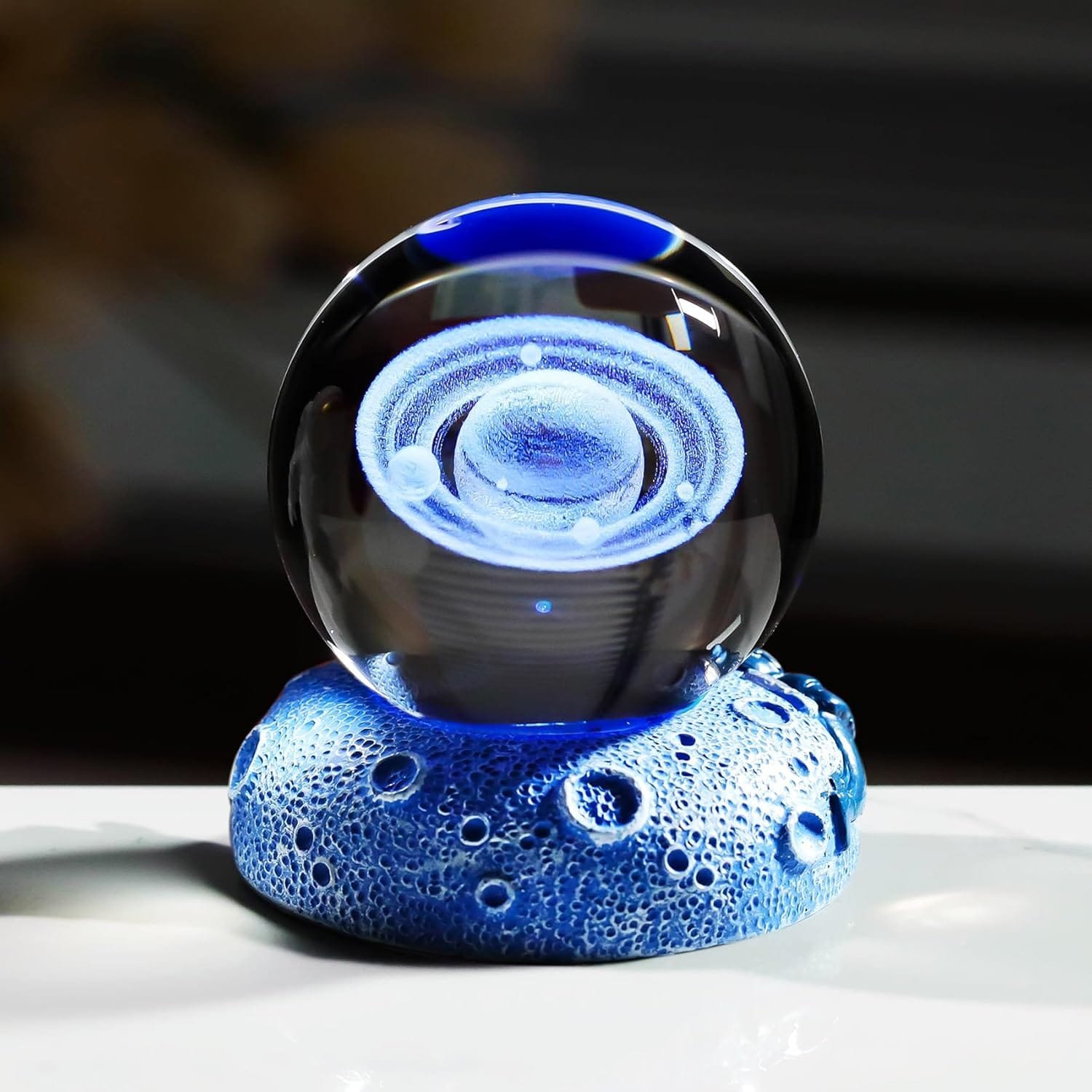 A glass orb with swirling blue patterns sits on a textured blue base, resembling a miniature galaxy or planet.