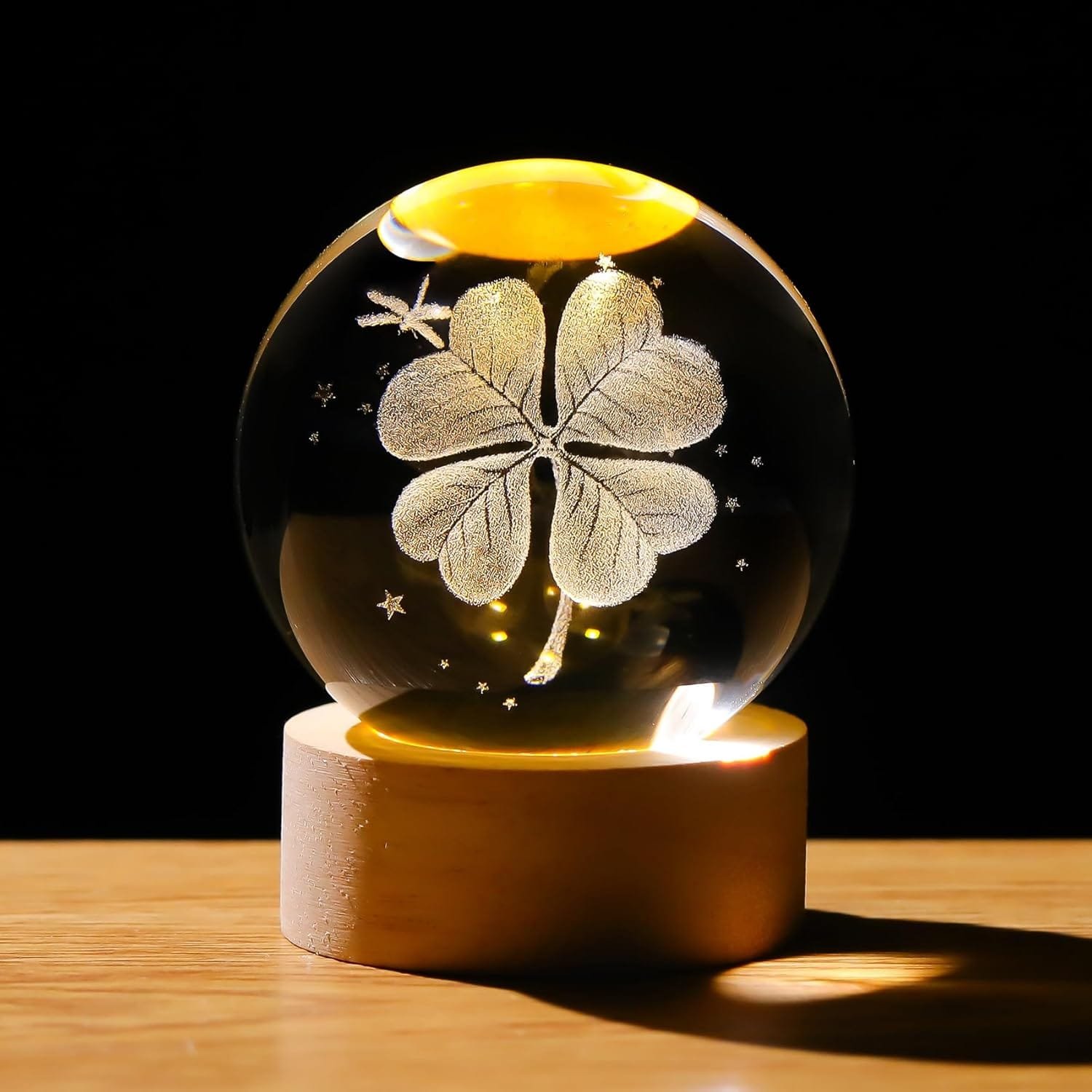 A crystal ball with a clover design inside, placed on a wooden base. The ball is illuminated, casting a warm glow.