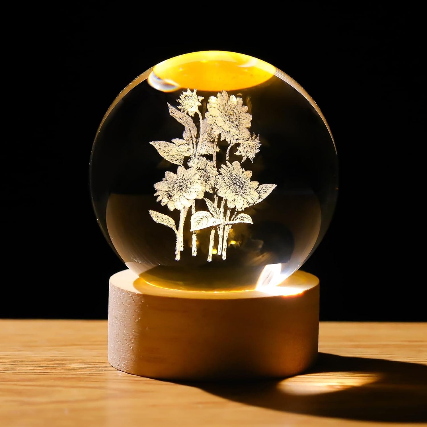 Glass orb with etched flowers, illuminated from below, on a wooden base.