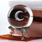 A crystal ball with an engraved crescent moon and stars sits on an ornate metal stand, next to a partially visible box with brown and white fabric.