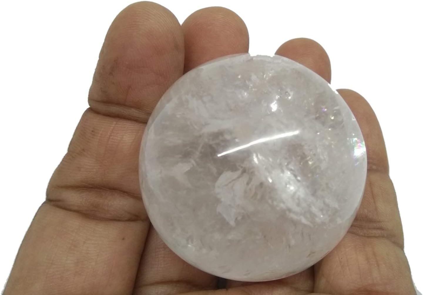 A clear, round crystal is being held in a person's hand against a plain background.