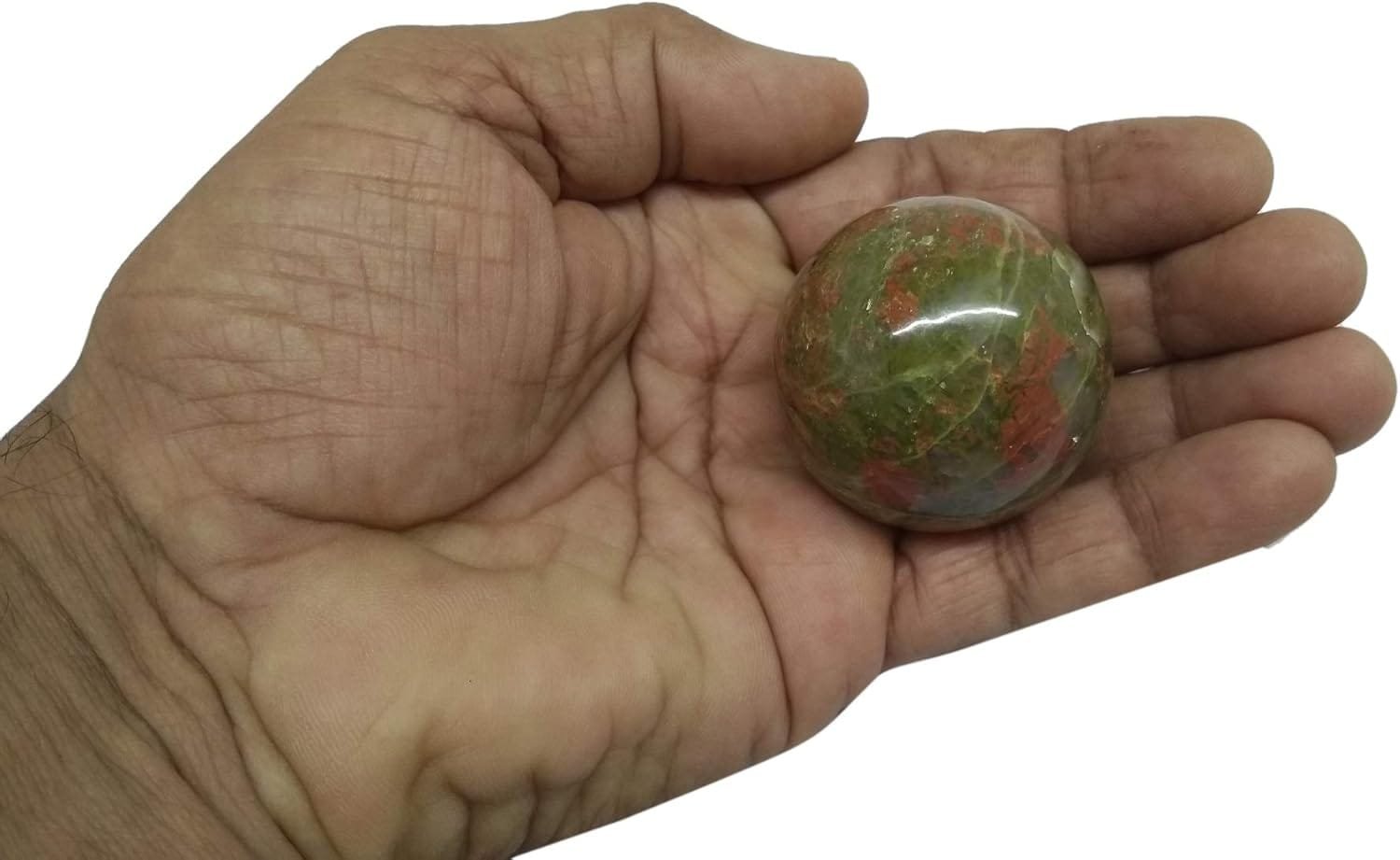 A hand holding a round, multicolored stone with green and red hues.