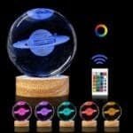 A crystal ball with a 3D Saturn inside, on a wooden stand. Below, five other colored crystal balls are displayed. A remote control and a color wheel are shown alongside.
