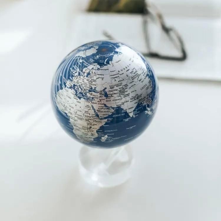 The Globe Metallic 4.5" is a compact metallic blue and white globe that stands on a clear base, showcasing parts of Europe, Africa, and Asia, with a pair of glasses softly out of focus in the background.