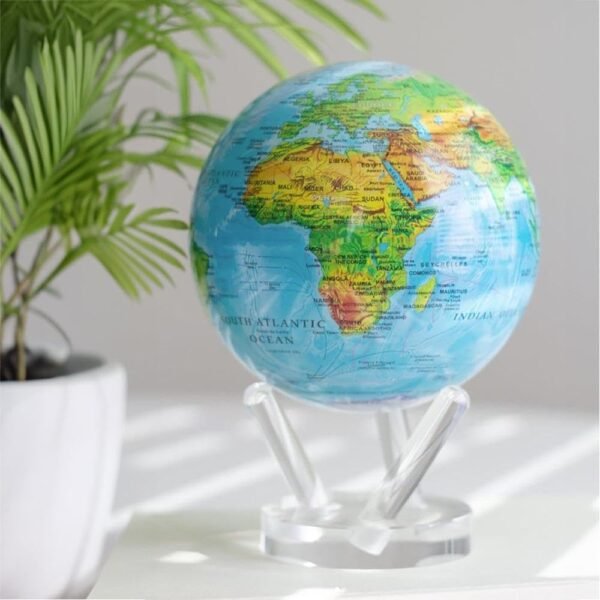 A *Globe Relief Map Blue 6"* sits on a clear stand beside a potted plant, showcasing regions of Africa, Europe, and the Atlantic Ocean in a well-lit room.