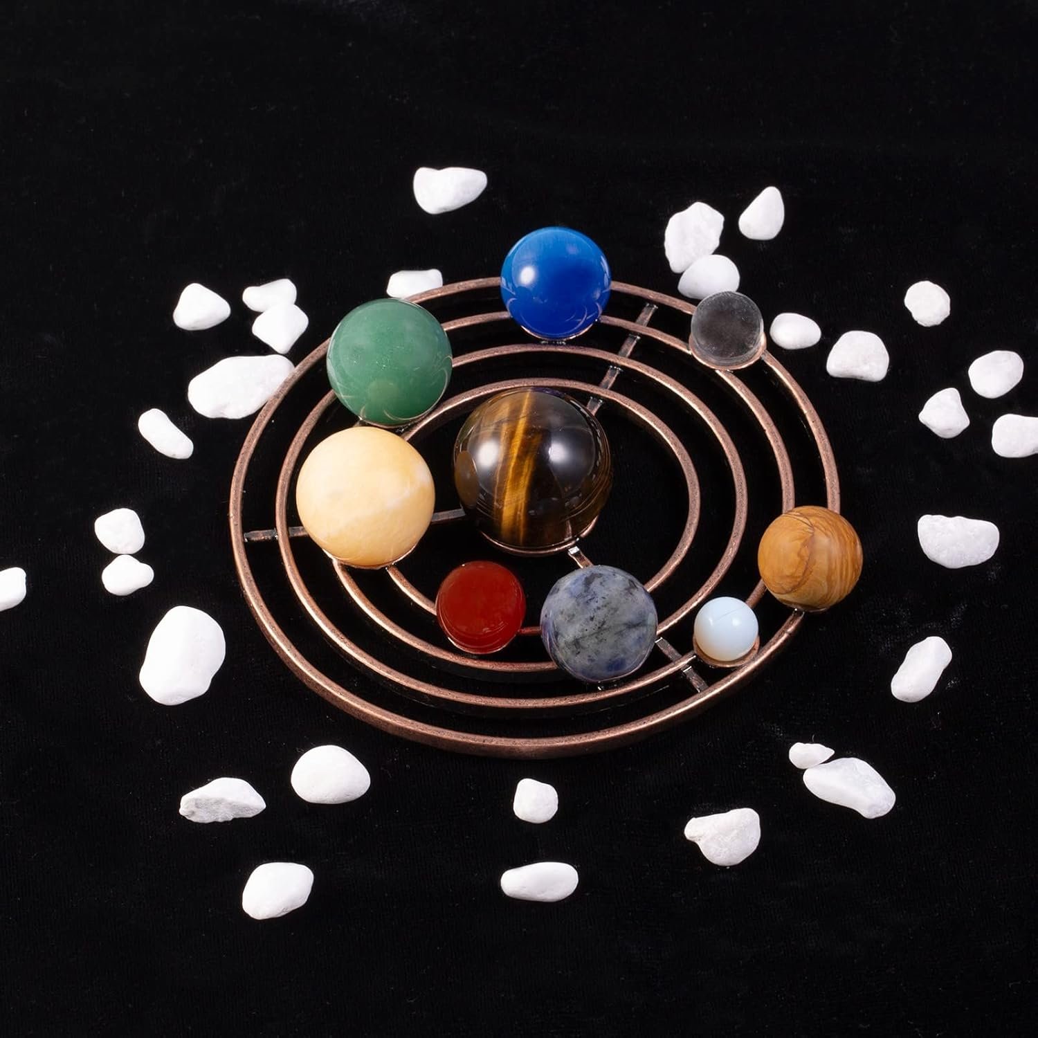 A model of the solar system with colorful spheres representing planets on a spiral stand, surrounded by small white stones on a black background.