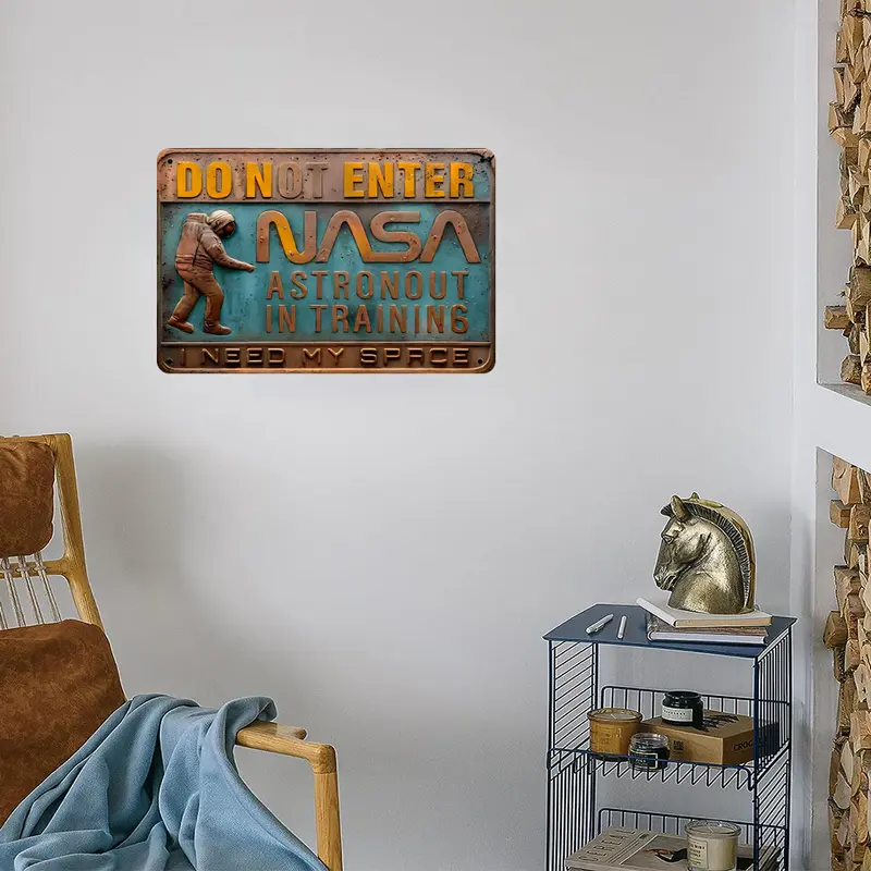 A cozy room has a chair, blanket, and metal shelf. A 3D Embossed Metal Sign Astronaut Training - Space Theme Decor on the wall reads "DO NOT ENTER, NASA ASTRONAUT IN TRAINING, I NEED MY SPACE," with an astronaut image that captures the space theme perfectly.