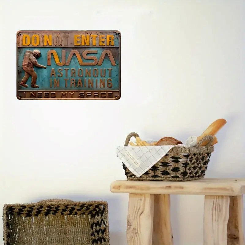 A basket of bread sits on a wooden table beneath the 3D Embossed Metal Sign Astronaut Training, labeled "Do Not Enter, NASA Astronaut In Training, I Need My Space," enhancing the quirky space theme decor.
