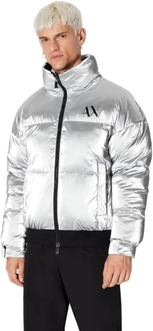 A person stands wearing a shiny silver puffer jacket with a logo on the chest, paired with black pants.