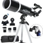 Black telescope on a tripod with accessories including two eyepieces, a Barlow lens, remote control, smartphone adapter, and a carrying bag.