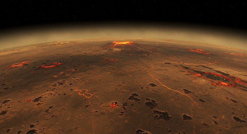 Aerial view of a volcanic landscape under a hazy atmosphere, with glowing lava flows and several craters on a barren, reddish surface.