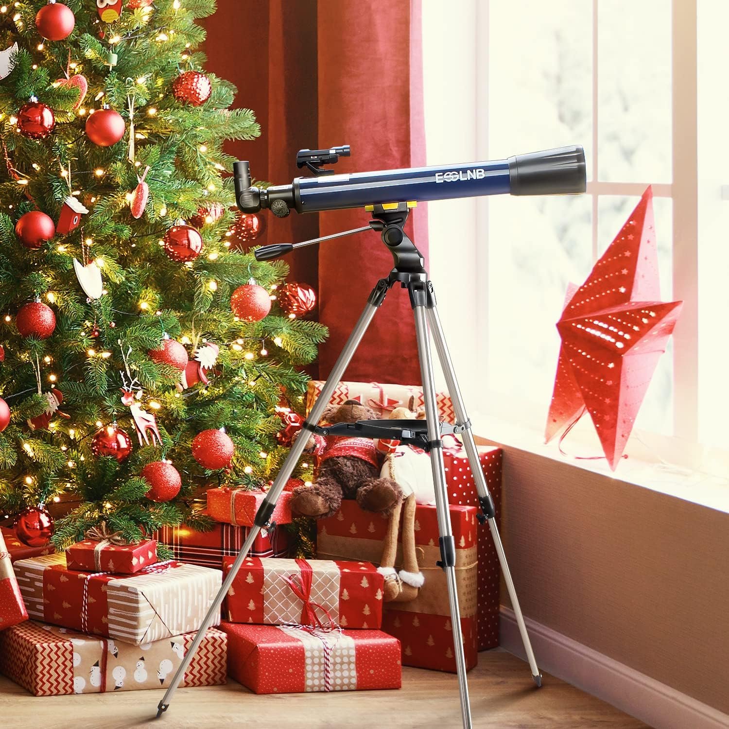 A telescope on a tripod stands next to a decorated Christmas tree with wrapped gifts and a large red paper star by a window.