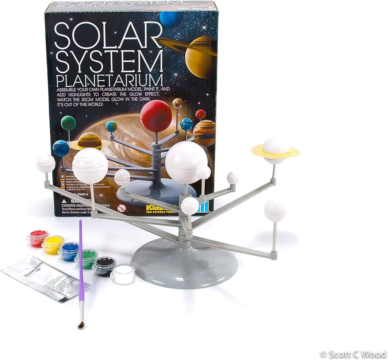 A solar system planetarium model kit is displayed with planets on rods, paint pots, a brush, and the kit box in the background.