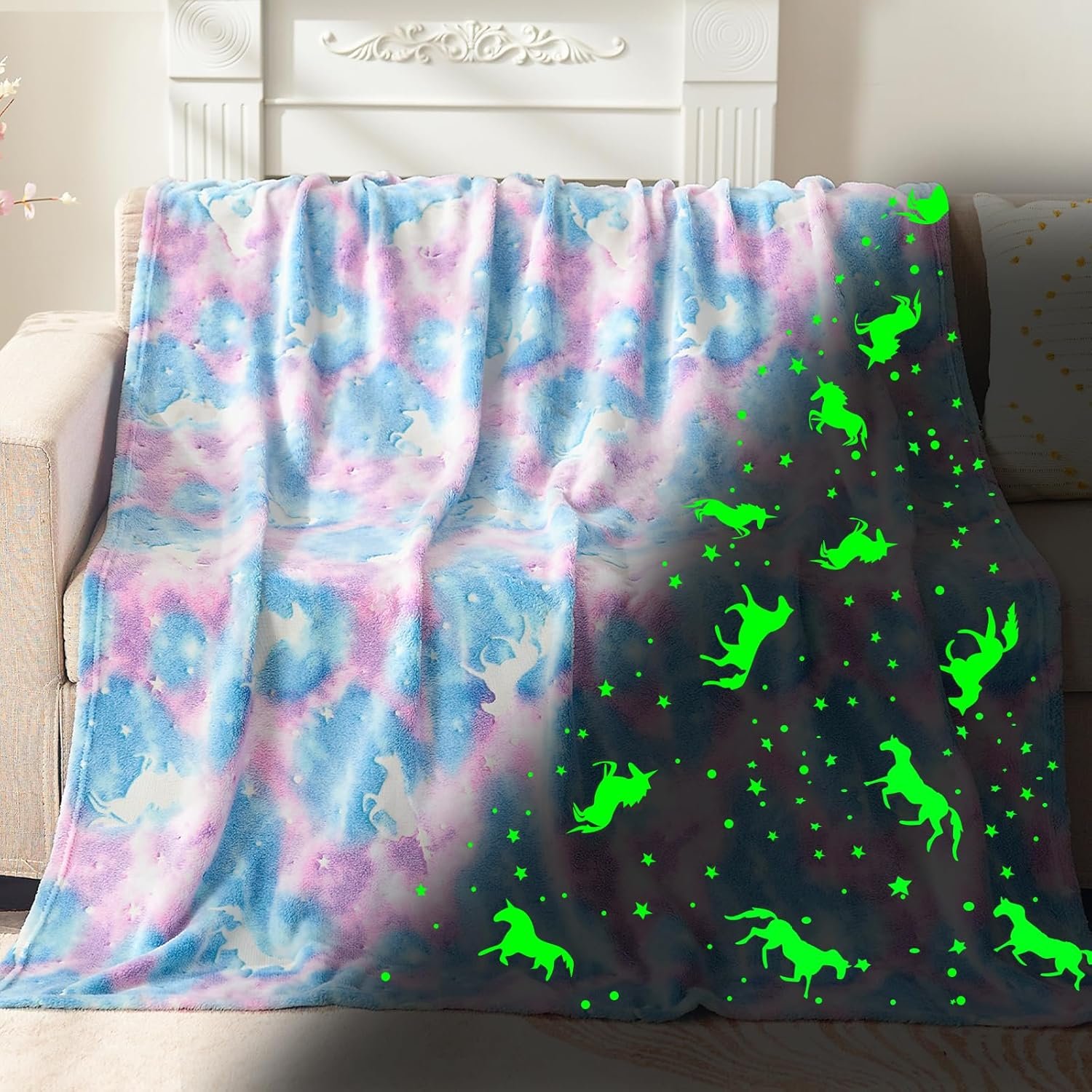 A pastel-colored blanket with unicorn and star patterns draped over a sofa; some unicorns and stars glow in green under dim light.