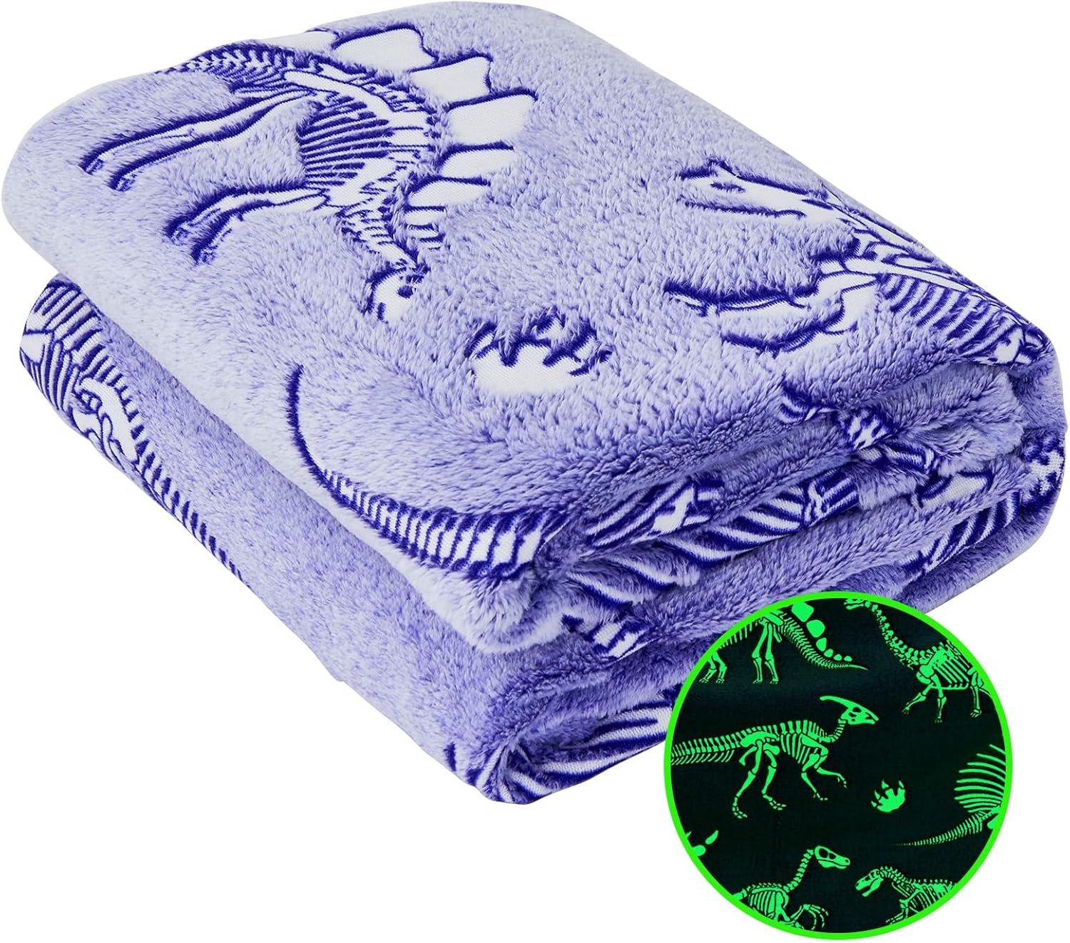A folded purple blanket with dinosaur skeleton patterns, shown glowing in the dark in an inset circle at the bottom right.