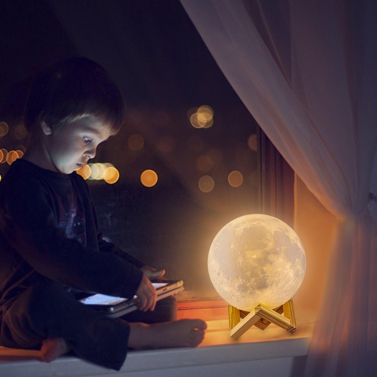 A child sits on a windowsill at night, illuminated by a tablet screen and a glowing moon-shaped lamp beside them.
