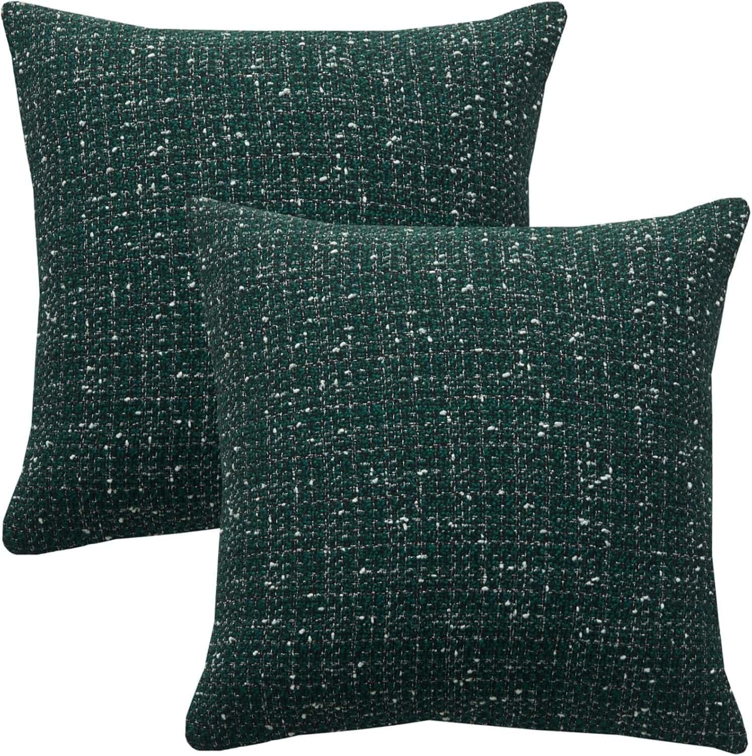 Two square, dark green throw pillows with a subtle white speckled pattern are placed overlapping each other against a plain white background.