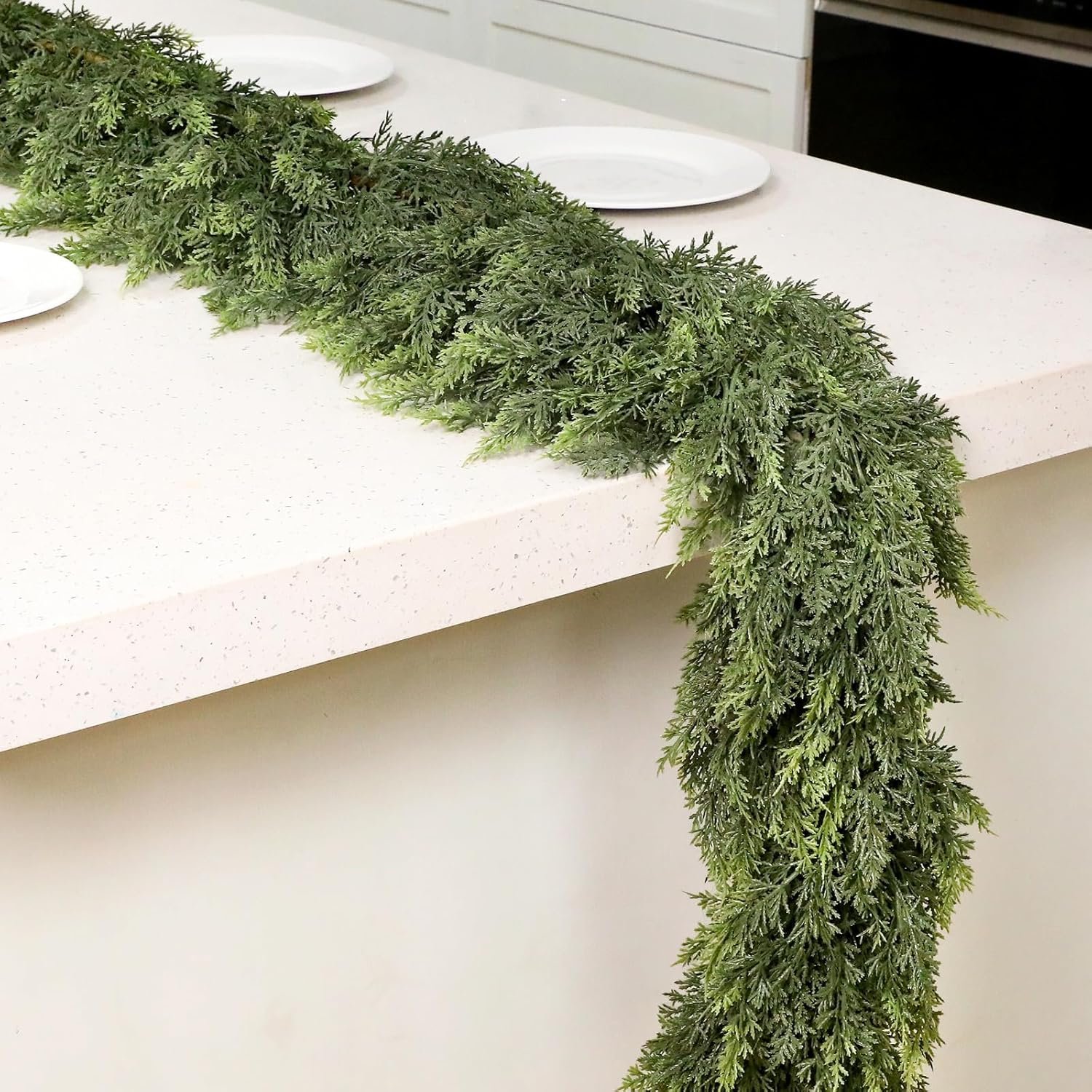 A long, green, artificial garland is draped across a white quartz countertop with white plates set along the edge.
