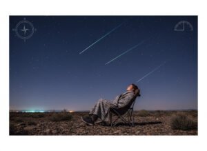A person wrapped in a blanket sits on a chair outdoors at night, watching a spectacular meteor shower as multiple meteors streak across the starry sky.