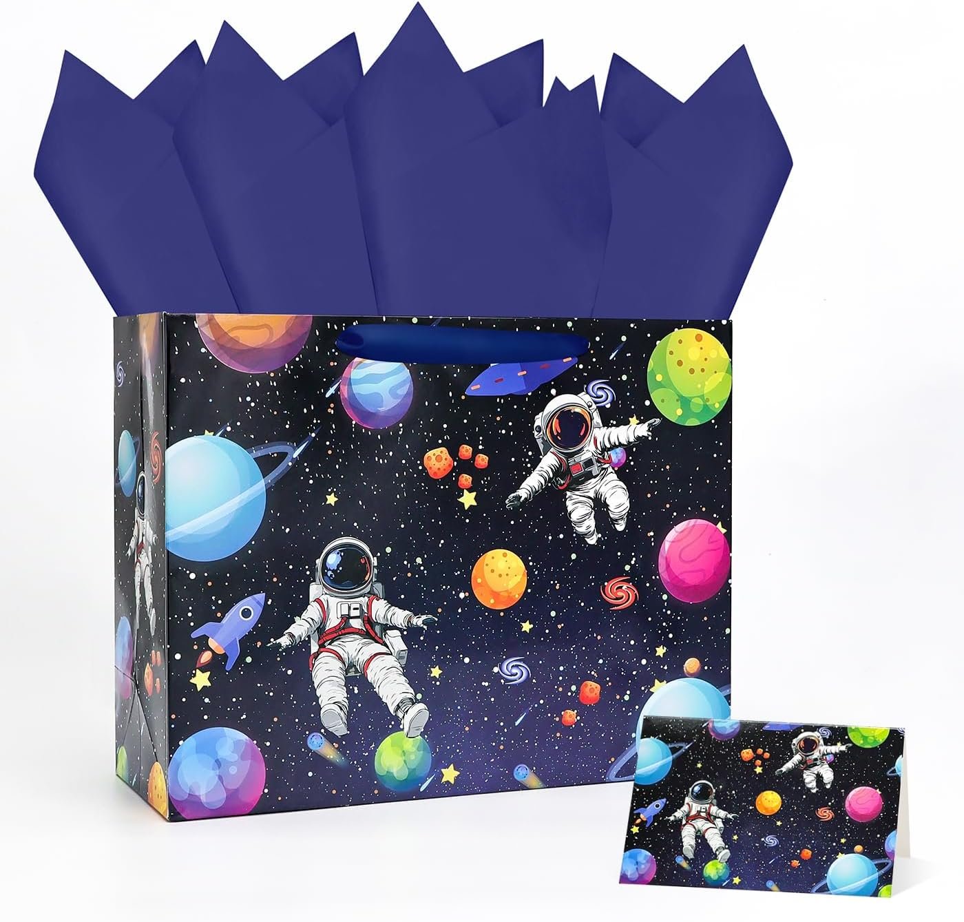 A gift bag with a space theme featuring astronauts, planets, and stars on a dark background, with dark blue tissue paper and a matching gift card.