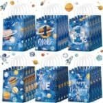A set of blue space-themed gift bags with planets, stars, rockets, and astronaut designs, some reading "One," the number "1," and "Happy Birthday.