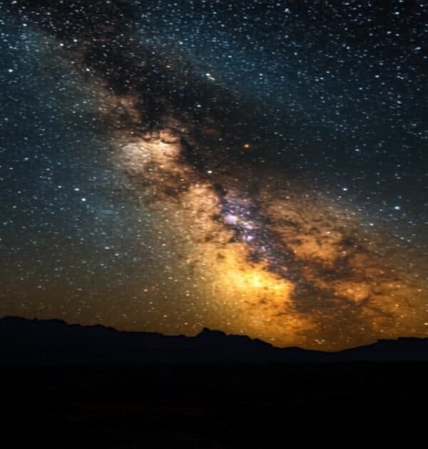 Milky Way galaxy arc glowing over dark rugged landscape at night