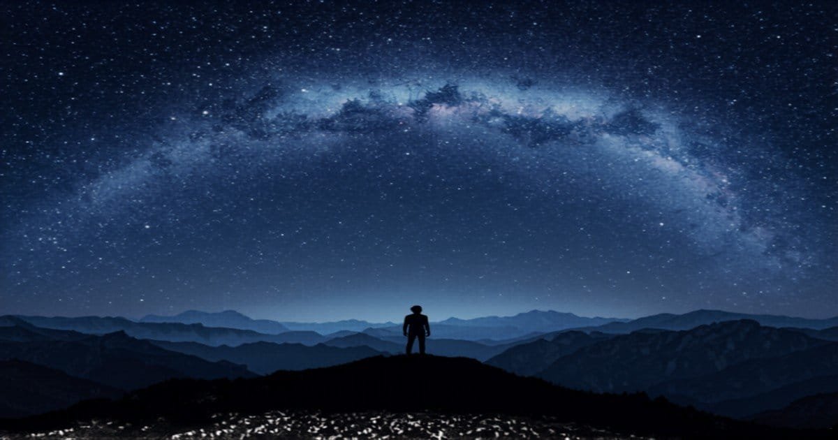 Silhouette of person stargazing under the Milky Way band in dark sky